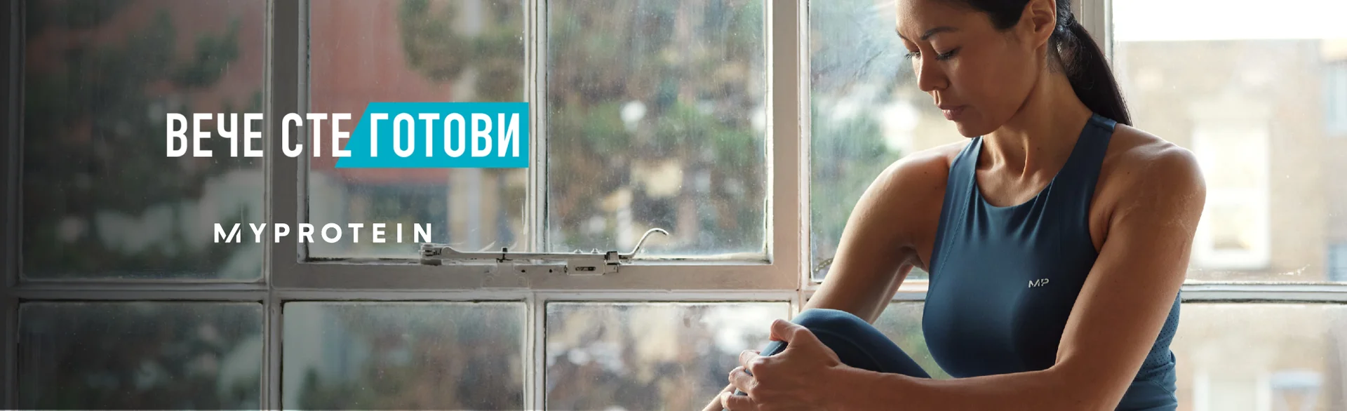 A woman wearing MP gym clothing sat on a window ledge stretching with the text 'You're Already Ready - MYPROTEIN' overlaying the image.